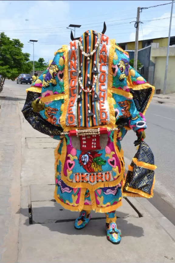 Egungun au costume de perles et de franges dorées, orné de lions et de motifs colorés, dans une rue